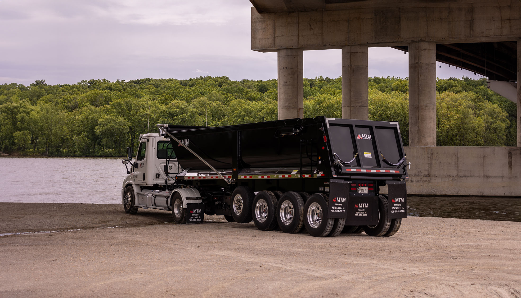 black quad end-dump trailer under a bridge
