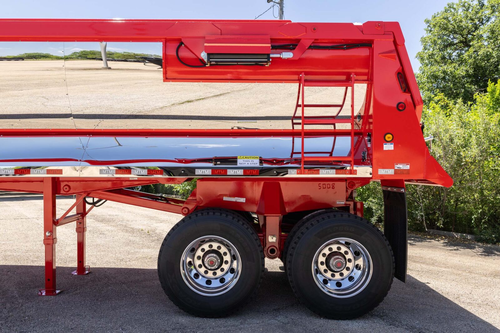 Red MTM quarter-frame end-dump trailer with chrome finish, side view