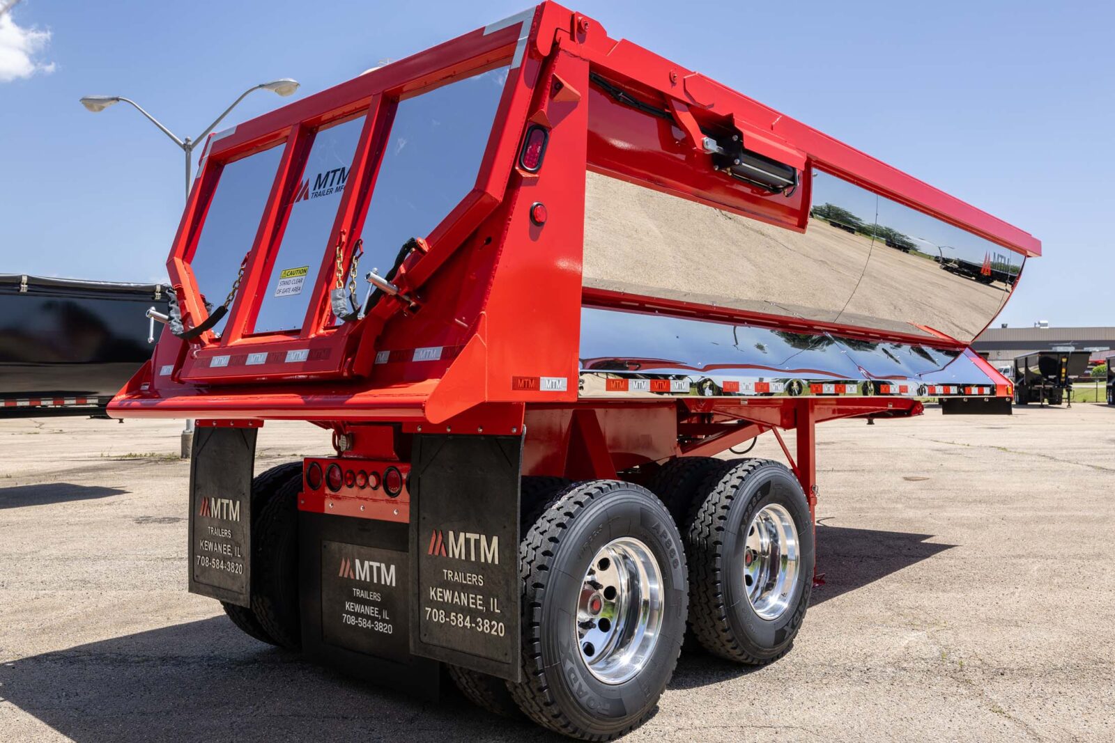 Red MTM quarter-frame end-dump trailer with chrome finish, side view