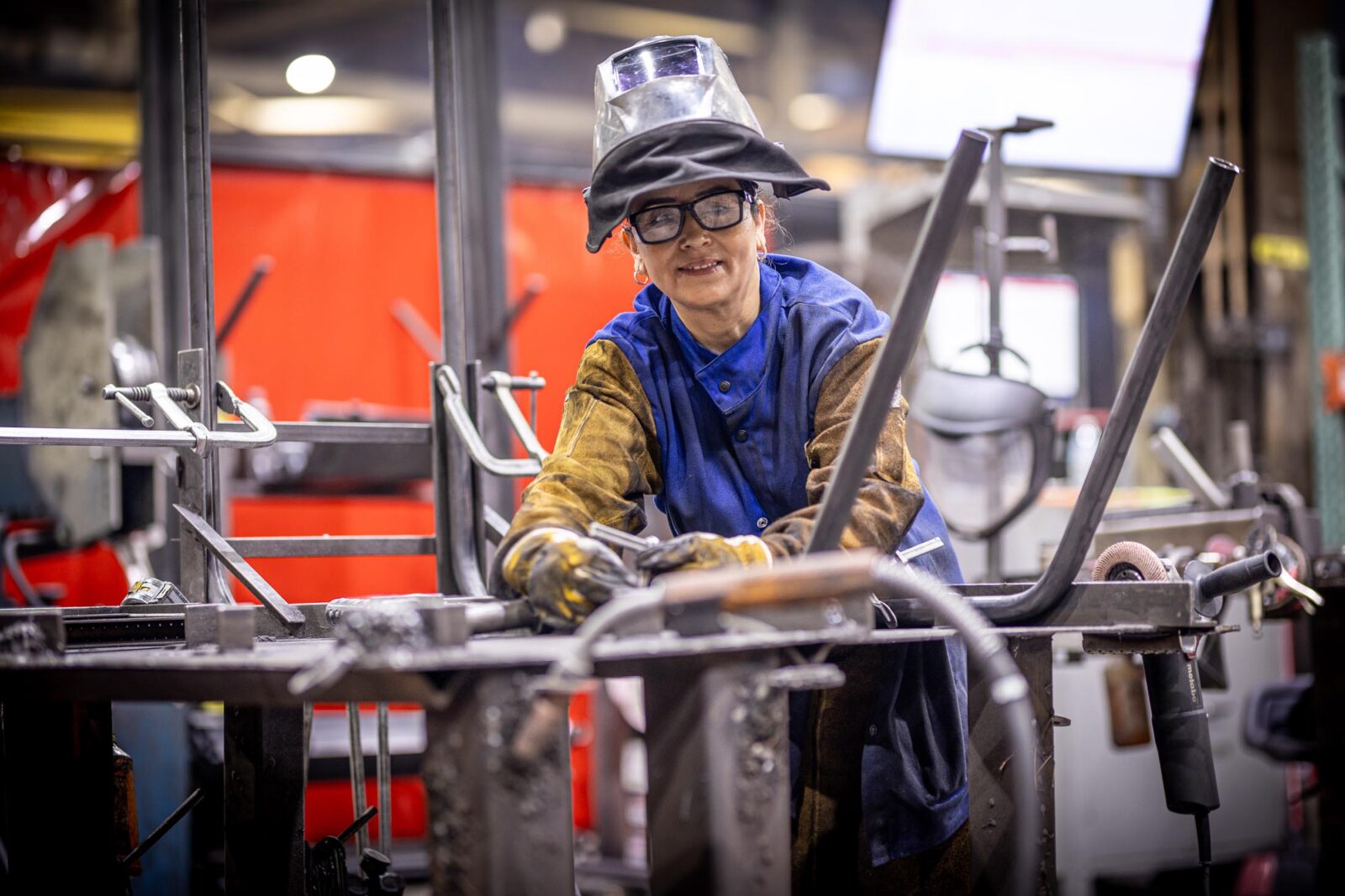 Woman wearing safety glasses and a welders helmet smiling and looking at the camera