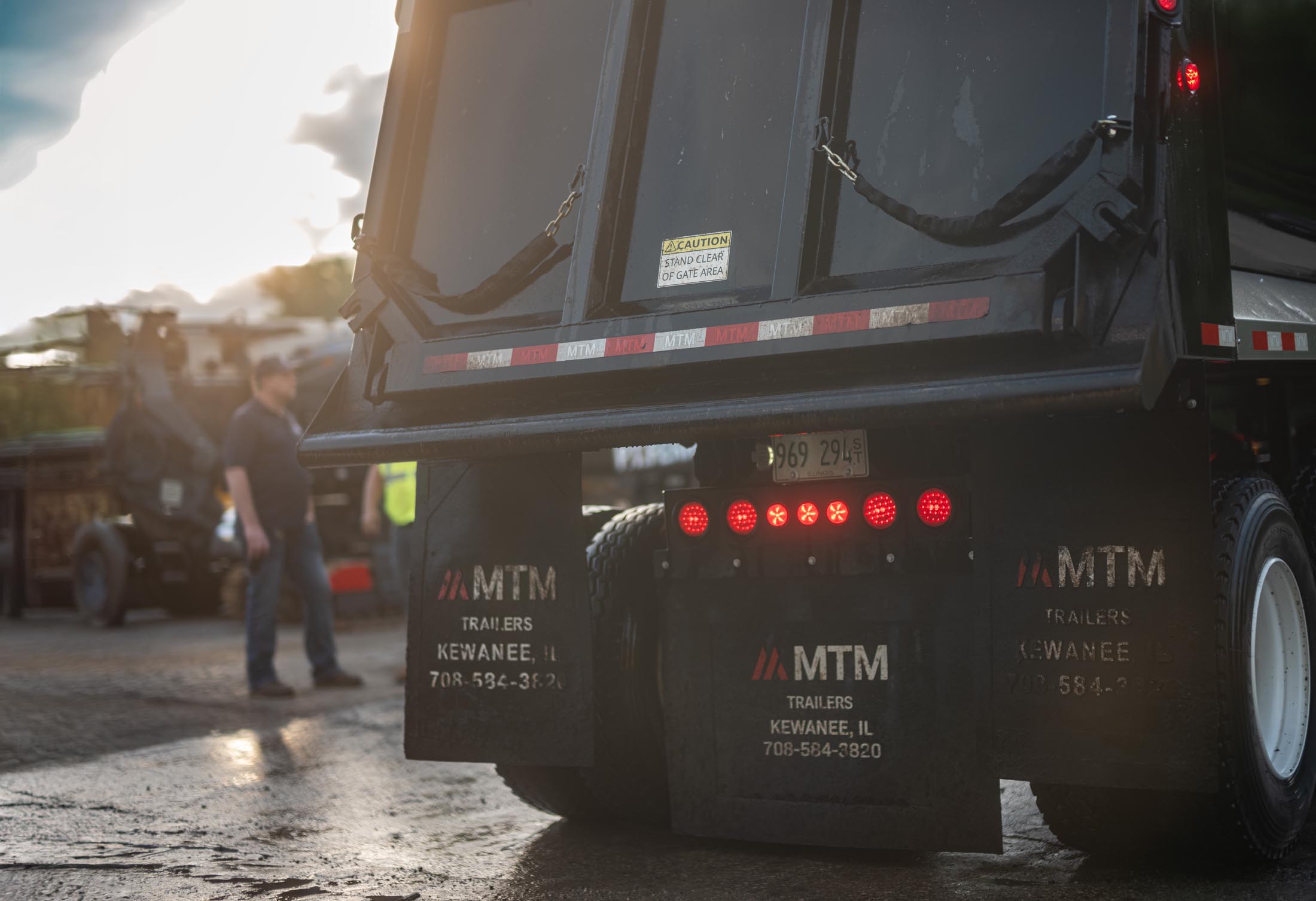 Black MTM trailer in a lot and with a driver standing in the background