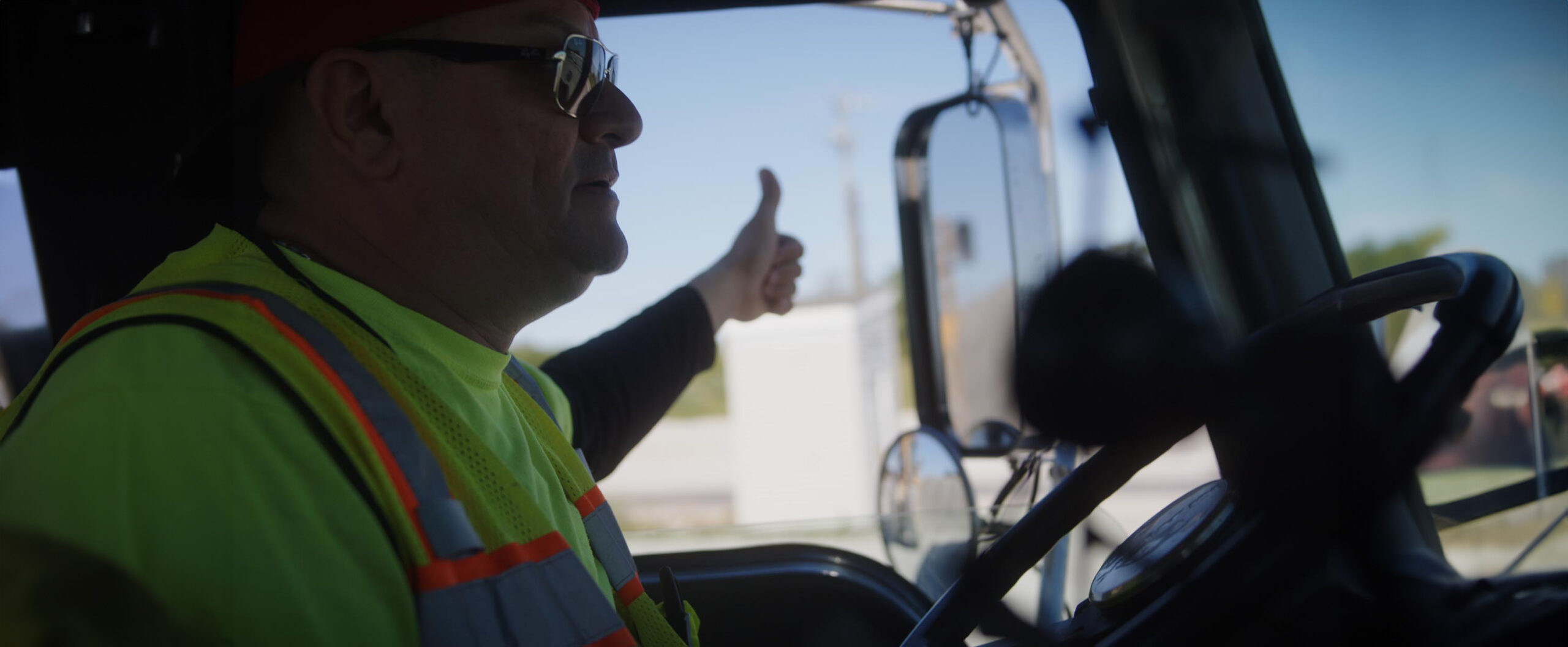 driver in a safety vest in the cab of his truck giving the thumbs up