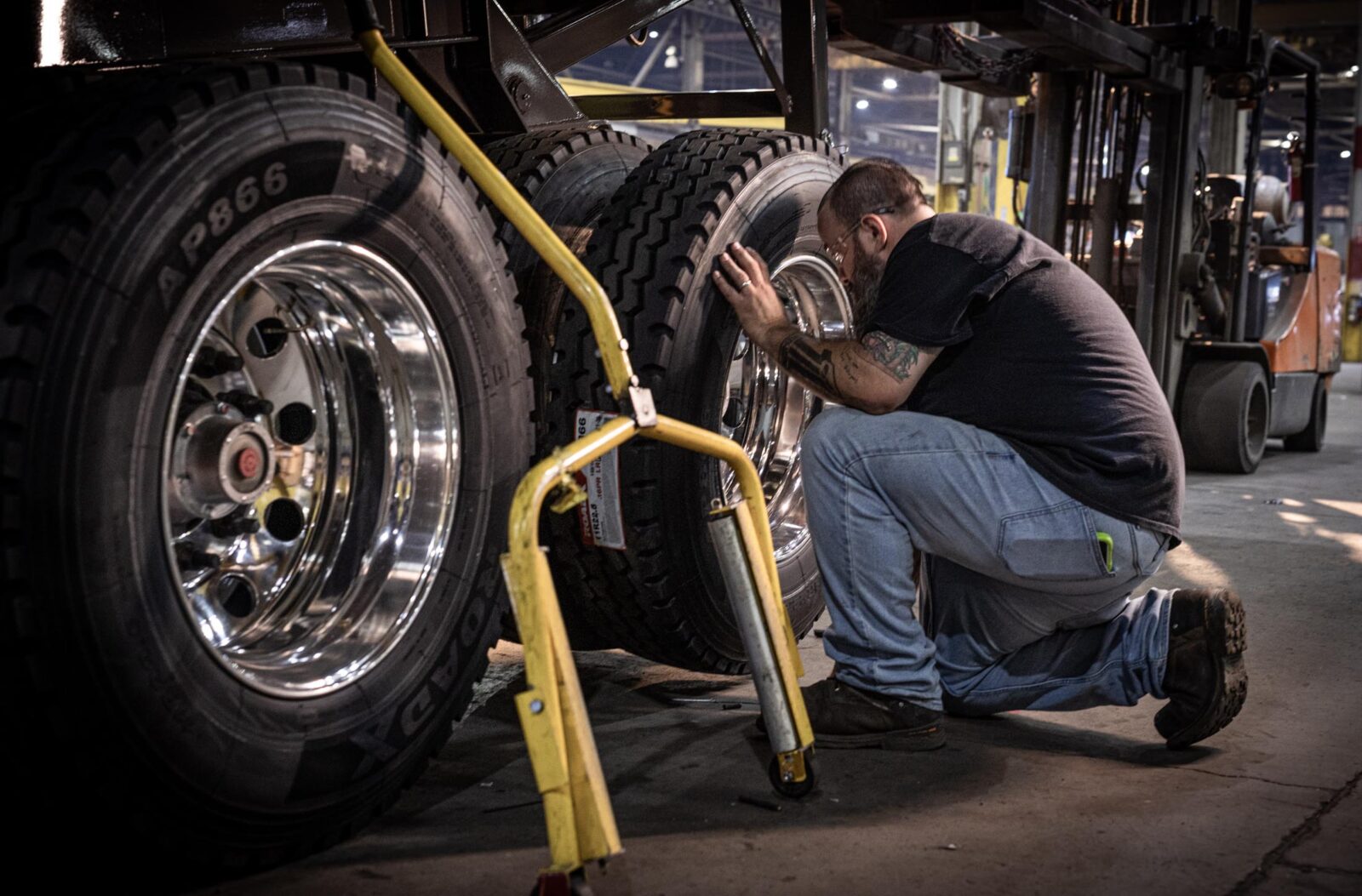 A man in a black t-shirt and jeans working on a trailer tire