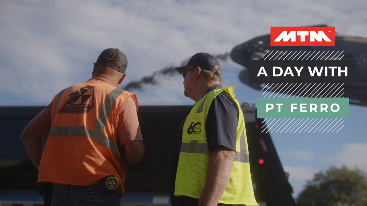 two men standing in front of an MTM end-dump trailer that's being filled with asphalt