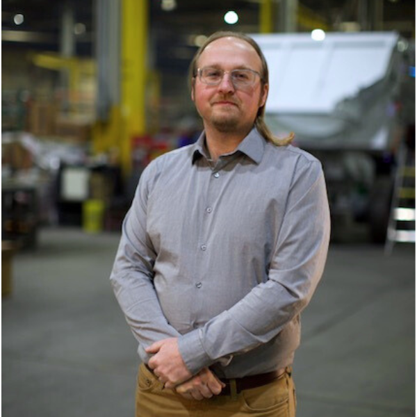 Man in a grey shirt standing in front of an end-dump trailer